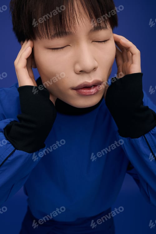Preview: Young handsome Asian man expressing emotion against a vibrant blue backdrop in a creative setting