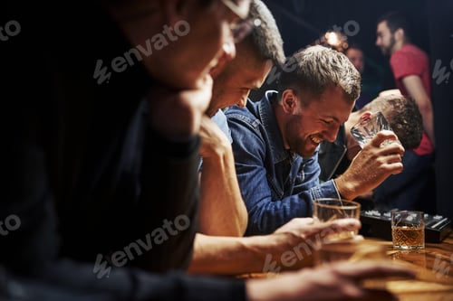 Preview: Side view. Friends resting in the pub with alcohol in hands. Having conversation