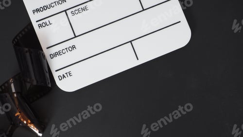 Preview: Small white clapper board and film roll on black background.