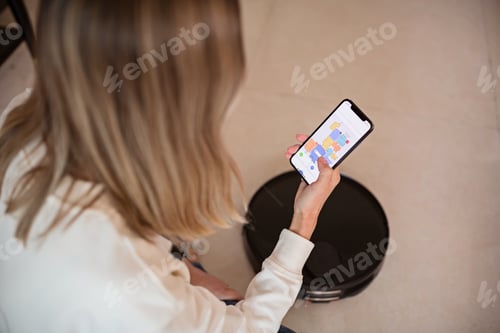 Preview: Robotic vacuum cleaner cleaning the room while woman relaxing. Woman controlling vacuum with remote