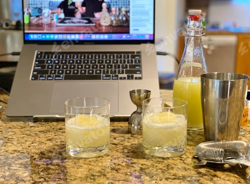 Preview: Two yellow cocktails on the counter surrounded by shaker and bar tools for a virtual tasting class
