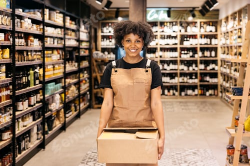 Preview: Smiling saleswoman carrying cardboard box in gourmet supermarket