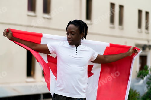Preview: a black male person holding a flag of canada outdoors, concept of patriotism and independence