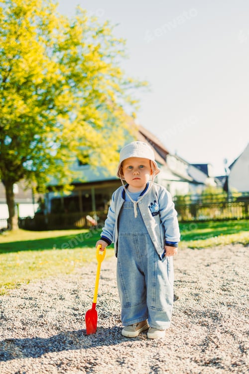 Preview: Toddler playing with a shovel in the sandbox on the playground. Boy playing in nature. 2 year old
