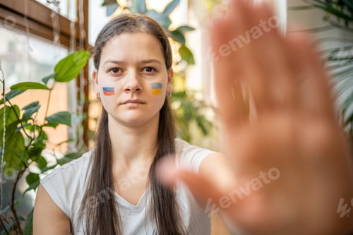 Vista previa: Portrait of young Russian-Ukrainian girl with the flag of Ukraine and Russia on her face.