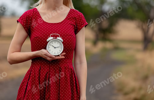 Preview: girl in a dress in polka dot with alarm clock on rural road