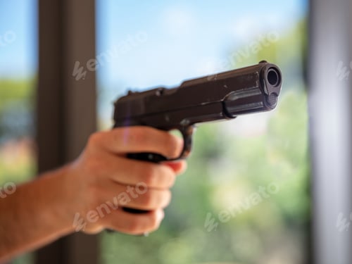 Preview: Male hand holding a pistol, blur nature background,