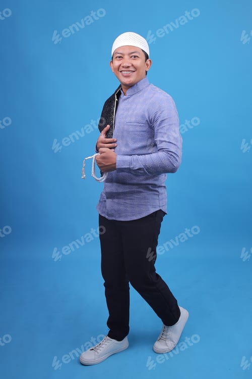 Preview: Portrait Of Smiling Young Man Holding Tasbih Walking And Smiling At Camera Over Blue Background