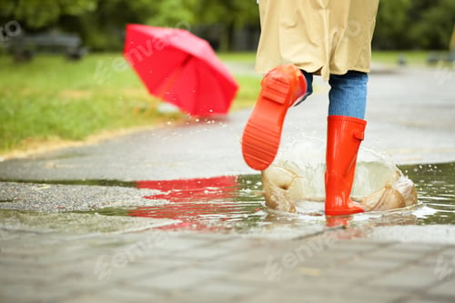 Preview: Woman in red rubber boots running after umbrella on street, closeup. Rainy weather