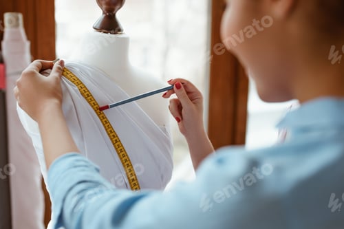Preview: Young designer with tape is measuring white dress. Designers studio