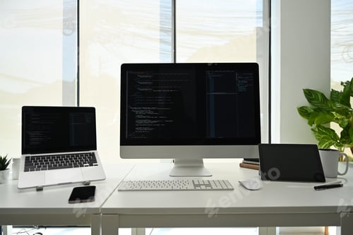 Preview: Computer monitors with programming code on white office desk at software development company.