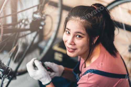 Preview: Asian woman happily replacing her bicycle chain at home in a DIY repair workshop.