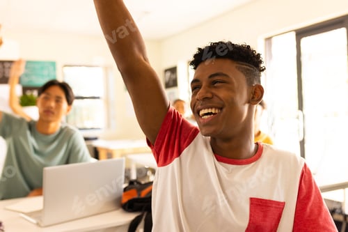 Preview: In high school, smiling teenage boy raising hand in classroom, participating actively