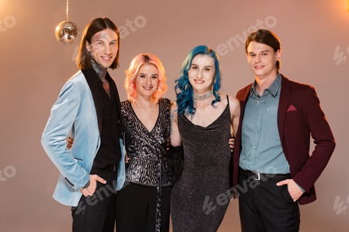 Preview: elegant and happy nonbinary friends looking at camera on beige background with pink lighting