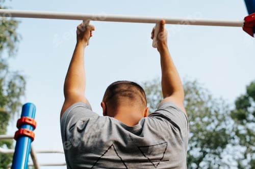 Preview: Athletic shaved man pulling himself up on horizontal bar, back view. Male sportsman training on