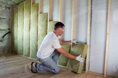 Preview: Worker in protective goggles and respirator insulating rock wool insulation
