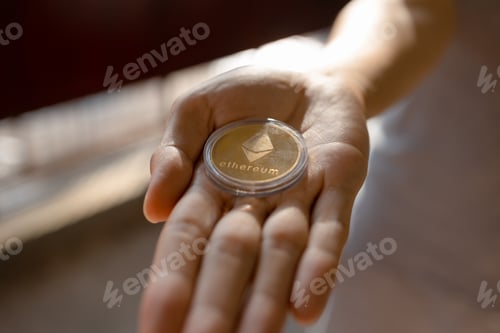 Preview: Young man holding ETH Ethereum coin on palm of hand