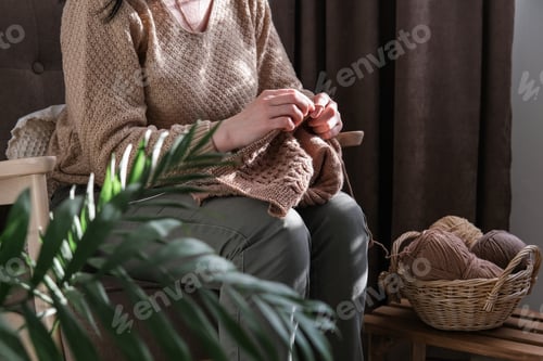 Vista previa: Mujer tejiendo mientras está sentada en una silla en un ambiente hogareño acogedor
