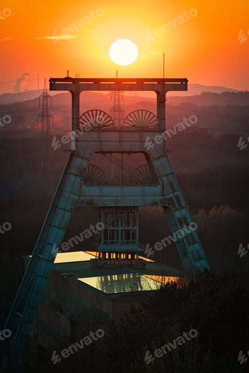 Preview: Vertical shot of a headframe tower with a golden sun setting in the background in Herten, Germany