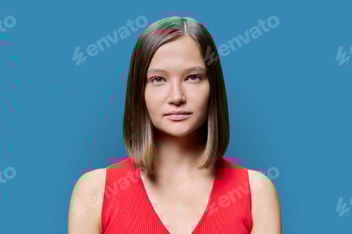Preview: Headshot portrait of young woman with natural makeup looking at camera on blue background