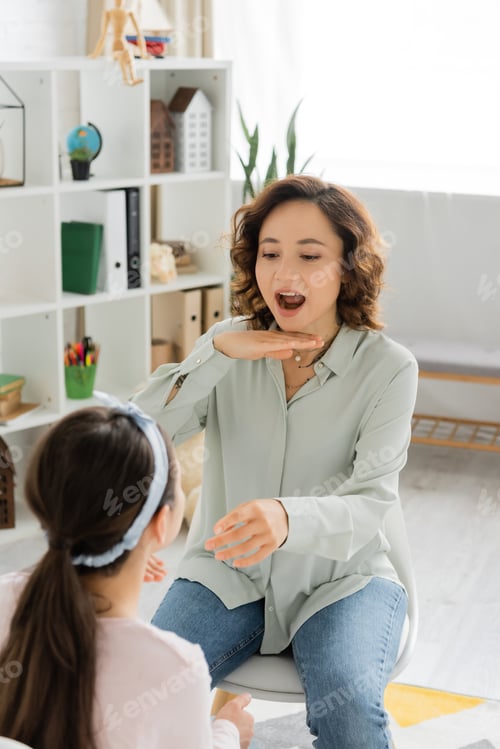 Preview: Speech therapist opening mouth and gesturing near blurred pupil in consulting room