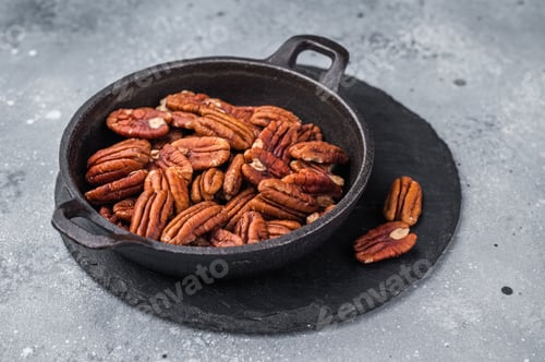 Preview: Brown pecan halves displayed in a cast iron pan resting on weathered wood against