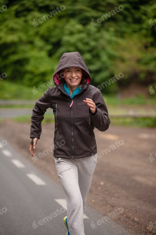 Preview: One Smiling Mature Woman, Jogging Outdoors On A Asphalt Road, In A Nature. Wearing Sport Clothing
