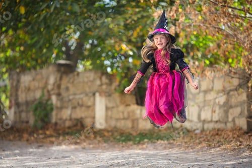 Preview: A little girl in a witch costume is jumping on the street. Halloween holiday. Copy space