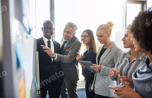Preview: Smiling colleagues strategizing together on a whiteboard in an office