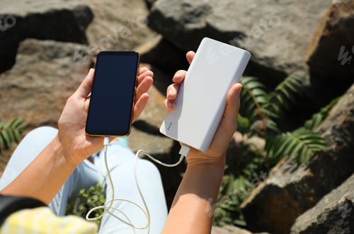 Preview: Woman charging smartphone with power bank on rocky mountain, closeup