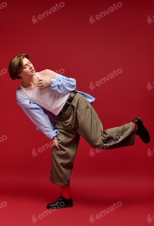 Preview: Stylish young man in trendy outfit poses against vibrant red backdrop