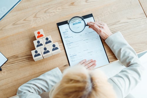 Preview: selective focus of blonde recruiter holding magnifier near clipboard