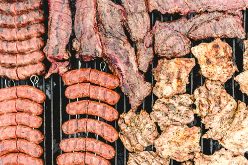 Preview: Sausage, pork and chicken roasted on a barbecue, seen from above.