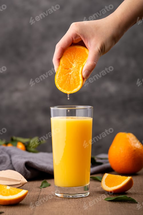 Preview: Glass of orange juice and a person squeezing an orange in it