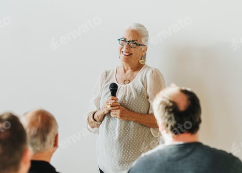 Preview: Cheerful elderly woman speaking on a microphone in a seminar