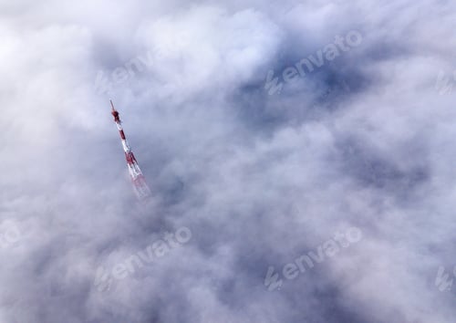 Preview: Aerial top view of foggy cloudy landscape with radio or TV antenna top on blue sky copy space