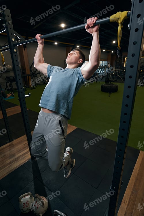 Preview: Focused calm young male gymnast doing pull-ups