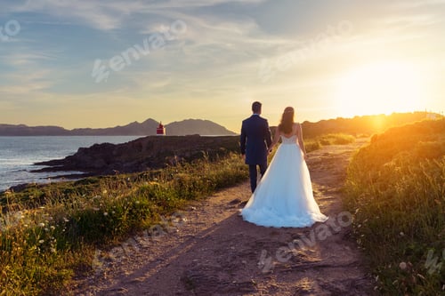 Preview: Portrait of groom and bride walking near the ocean at sunset