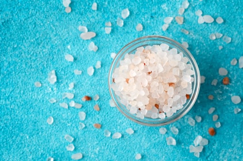 Preview: bowl of pink salt with scattered crystals on blue background