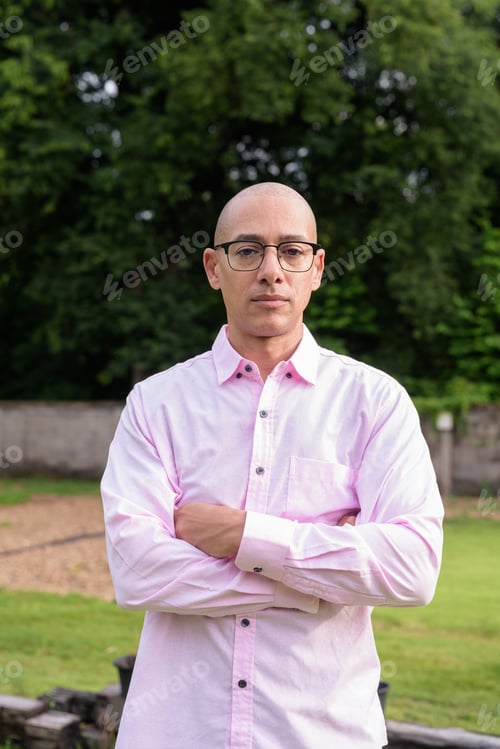 Preview: Bald Hispanic man wearing pink casual business shirt and eyeglasses outdoors with arms crossed