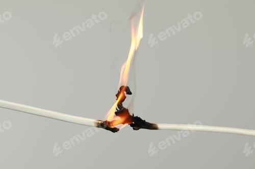 Preview: Inflamed white wire on grey background, closeup. Electrical short circuit