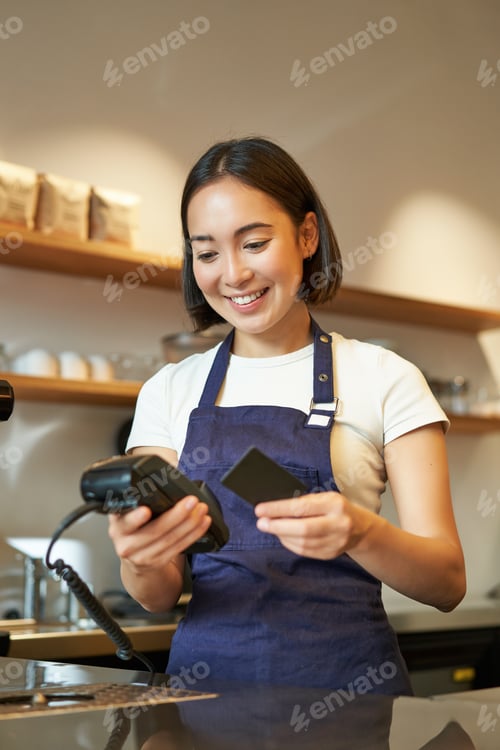 Preview: Portrait of smiling asian barista, coffee shop employee using POS terminal and credit card, helps