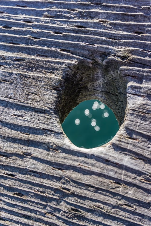 Preview: A Closeup Shot Of A Hole In A Wooden Pier Railing With Light Reflected From Below.