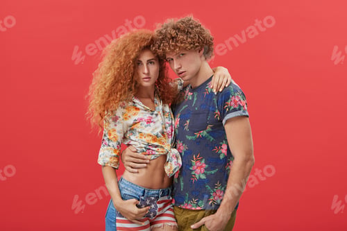 Preview: Young handsome guy with curly bushy hair wearing fashionable T-shirt hugging his slim pretty girlfri