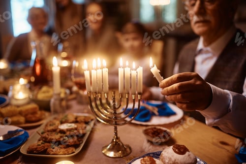 Preview: Close up of senior man lighting menorah during family dinner on Hanukkah.
