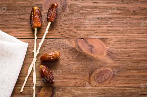 Preview: Sweet dried dates fruit put on sticks for eating on a wooden table. Top view