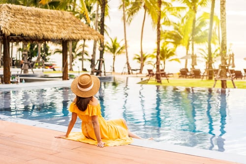 Preview: Young woman traveler relaxing and enjoying the sunset by a tropical resort pool