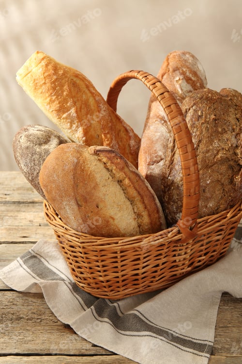 Preview: Different loaves of fresh bread in basket on wooden table, closeup
