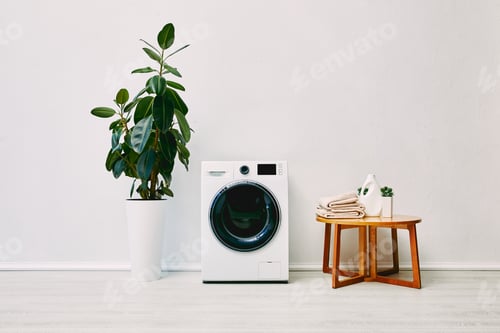 Preview: green plant near modern washing machine, coffee table with towels and detergent bottle in bathroom
