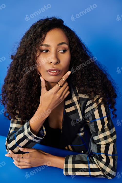 Preview: Elegant woman with curly hair poses thoughtfully against a vibrant blue background